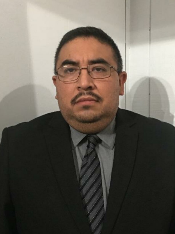 Photo of Jose Jimenez in a black suit with a grew shirt and tie